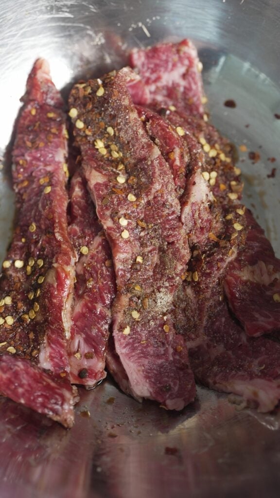 steak in mixing bowl with seasoning