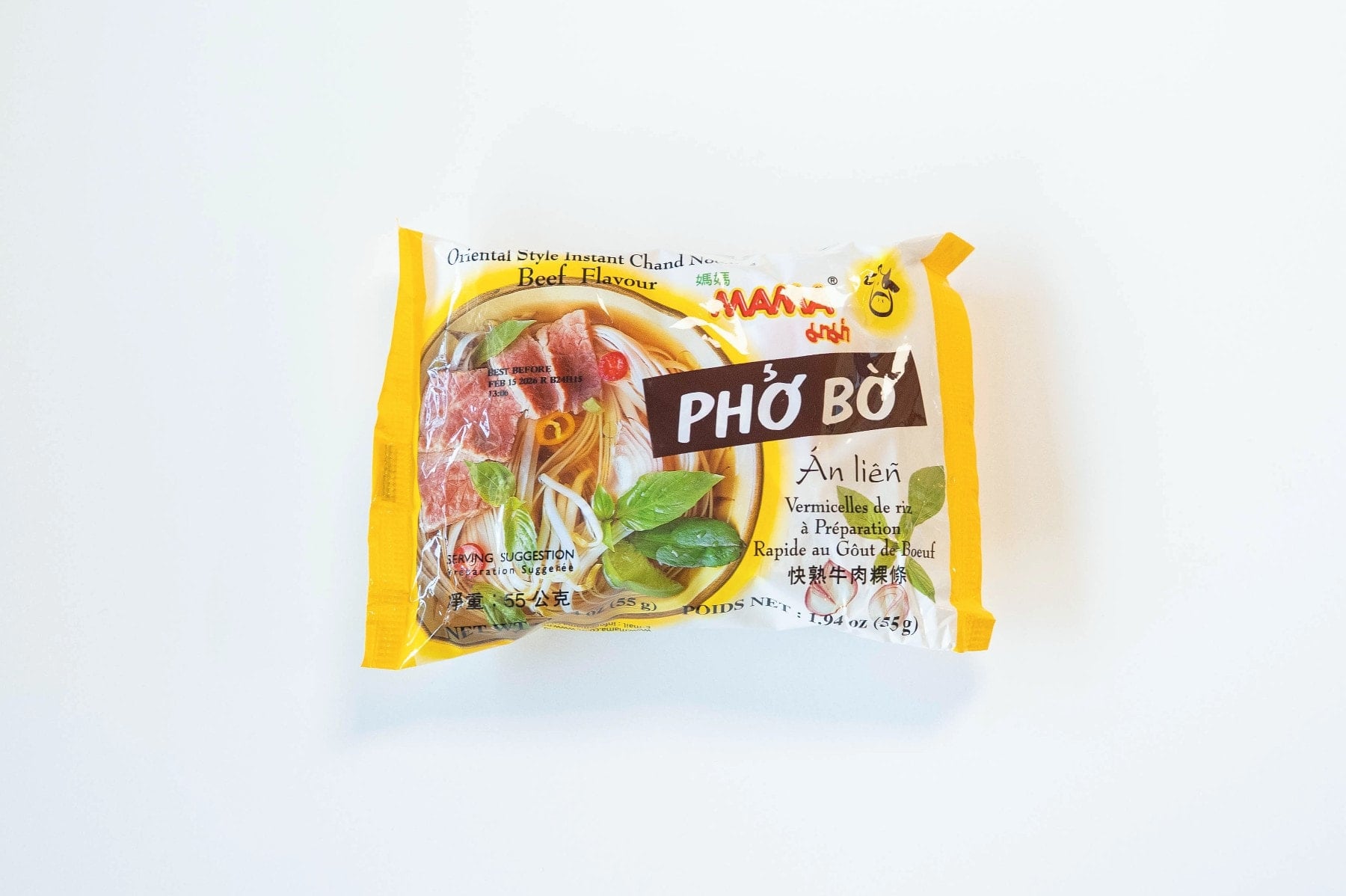 The yellow and red package of MAMA Phở Bò Beef Noodle Soup on a white surface, showing the small red MAMA logo at the top right, "Oriental Style Instant Chand Noodles" in white, "Beef Flavour" underneath, "PHỞ BÒ" in bold white text on a black banner, "Ăn liền" (instant) in red script, and a photo of finished pho with sliced beef, basil, chili, and flat white rice noodles.