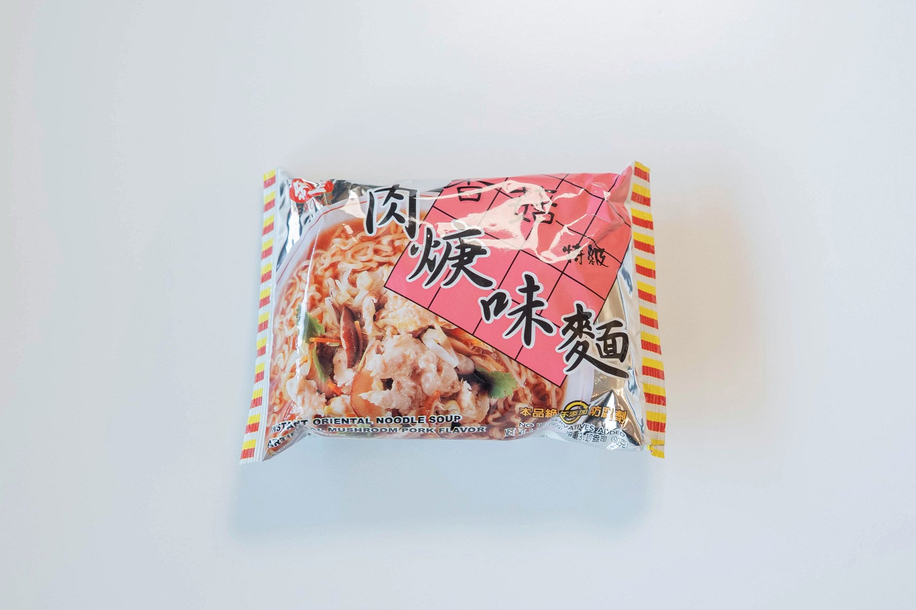 The Ve Wong Mushroom Pork Instant Noodle Soup package on a white surface, showing a silver foil background with red and yellow striped edges, a bold pink grid with black Chinese characters reading 香菇肉焿味麵 (Xiang Gu Rou Geng Wei Mian / Mushroom Pork Paste Flavor Noodle), and a serving suggestion of noodles in a thickened broth with pork bits and vegetables.