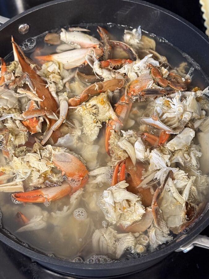 A close-up of blue crab shells being boiled in a large pot, with some crabs halved