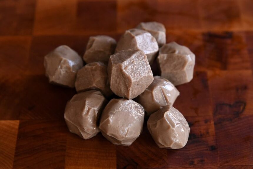 A pile of whole, smooth, and firm Vietnamese beef meatballs (bò viên) ready for slicing, resting on a dark walnut end-grain cutting board.