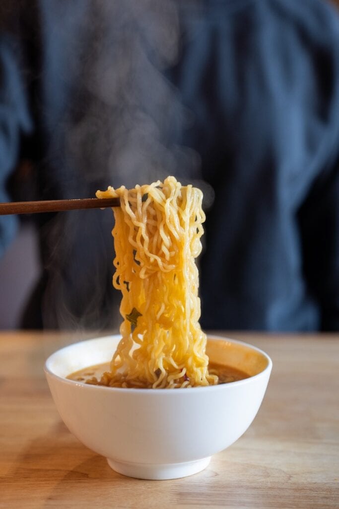 Nongshim Shin Ramyun Spicy Noodle Soup being lifted with chopsticks showing noodle texture