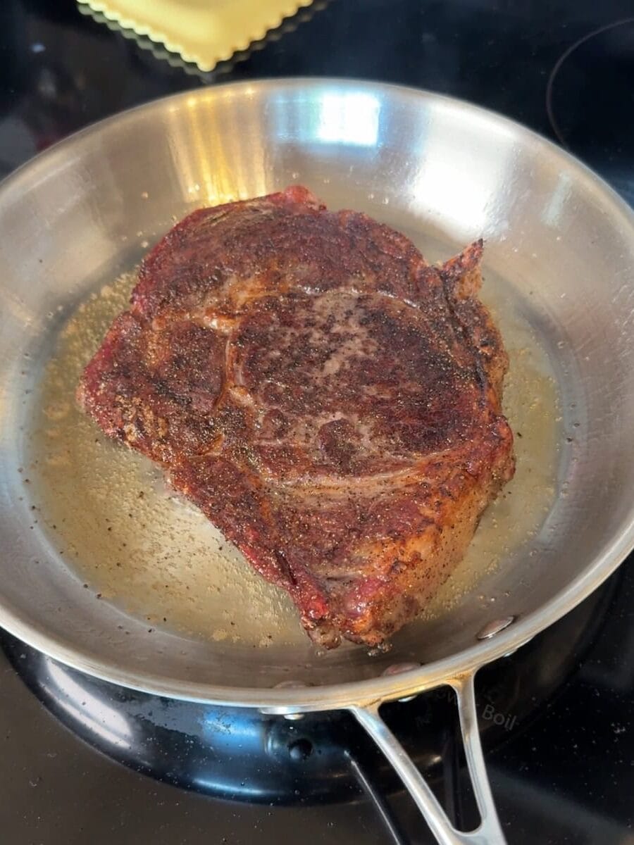 pan-seared ribeye steak cooking in stainless steel pan