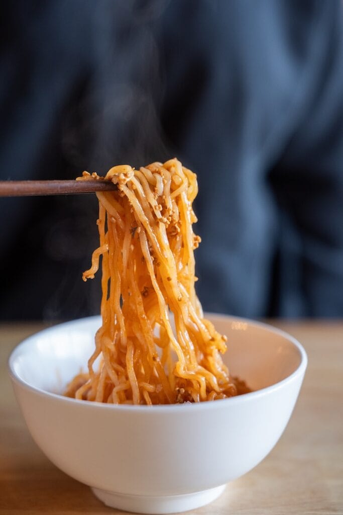 Samyang Buldak SWICY Sweet & Spicy Ramen being lifted with chopsticks showing noodle texture