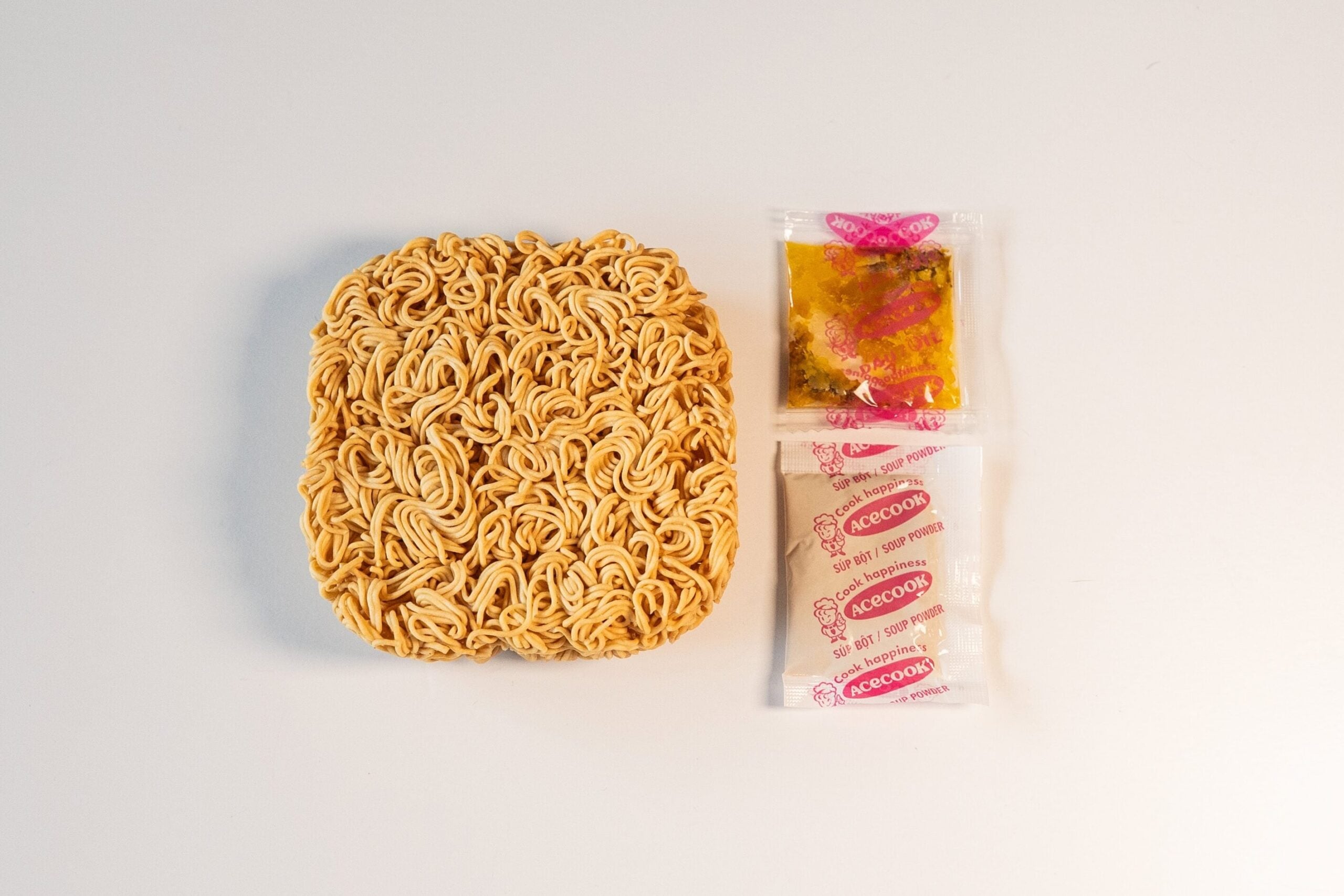 The contents of a Hao Hao noodle pack, showing the square block of thin dried noodles next to two seasoning packets.