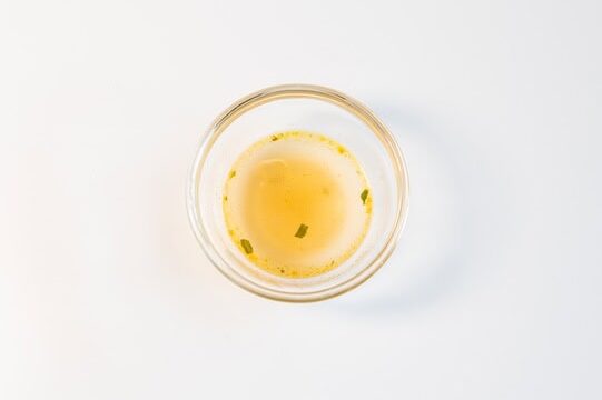 A small glass ramekin containing the clear, light-colored broth of the Hao Hao Hot and Sour Shrimp ramen.