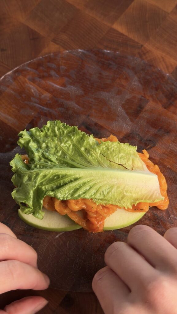 A green leaf lettuce leaf tucked over the creamy noodles to shield the rice paper from moisture