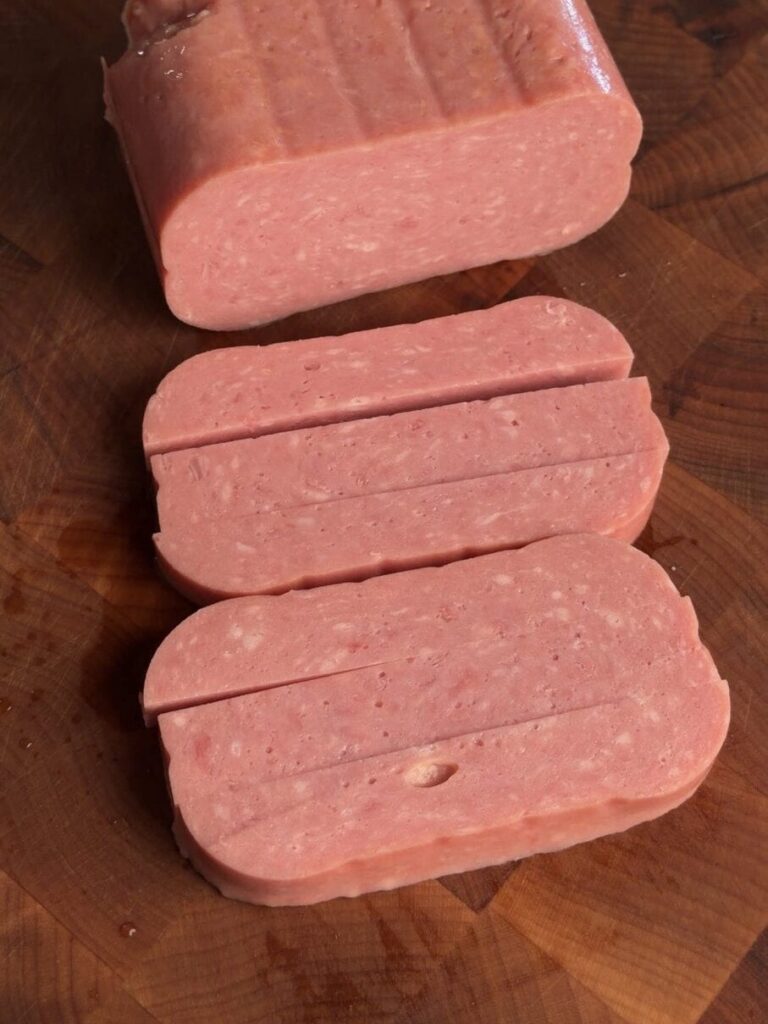 A block of Spam sliced into long uniform rectangles on a wood cutting board