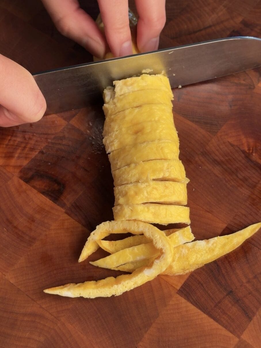 Slicing a rolled paper-thin egg sheet into thin egg ribbons with a chef knife