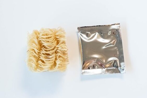 The contents of the Lotus Foods Tom Yum Rice Ramen Noodle Soup cup laid out on a white surface, showing a notably small rectangular block of organic brown rice ramen noodles on the left and a single silver foil seasoning packet on the right, both notably smaller than typical instant noodle contents.