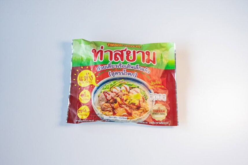 The green and red package of Thasiam Instant Dried Rice Stick Noodles with Spicy Sauce (Waterfall Formula) on a white surface, showing THASIAM NOODLES in white at the top, the brand name เธเนเธฒเธชเธขเธฒเธก in large red and white Thai script, a เธเนเธงเธขเนเธเธตเนเธขเธงเนเธฃเธทเธญเนเธชเนเธเนเธฅเนเธเนเธซเนเธ (dried thin boat noodle) Thai subtitle, a red STIR FRIED / เนเธซเนเธ callout, a เธชเธนเธเธฃเธเนเธณเธเธ (Waterfall Formula) tag, a photo of the finished dark dry noodles topped with beef and crispy bits, and a small THASIAM STREET FOOD badge.