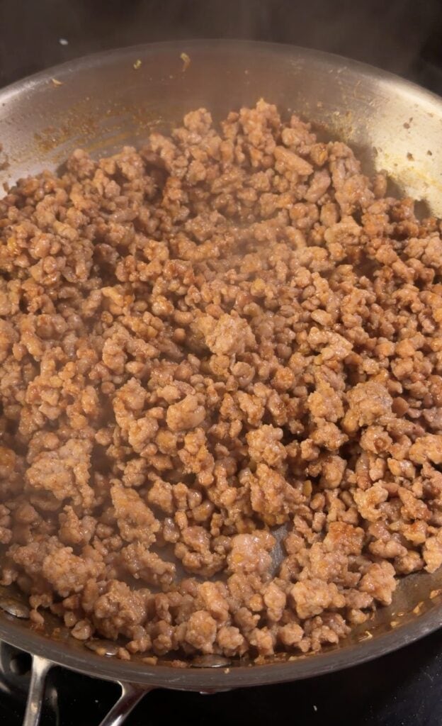 Seasoned ground pork cooking in a skillet, glossy and broken into small pieces