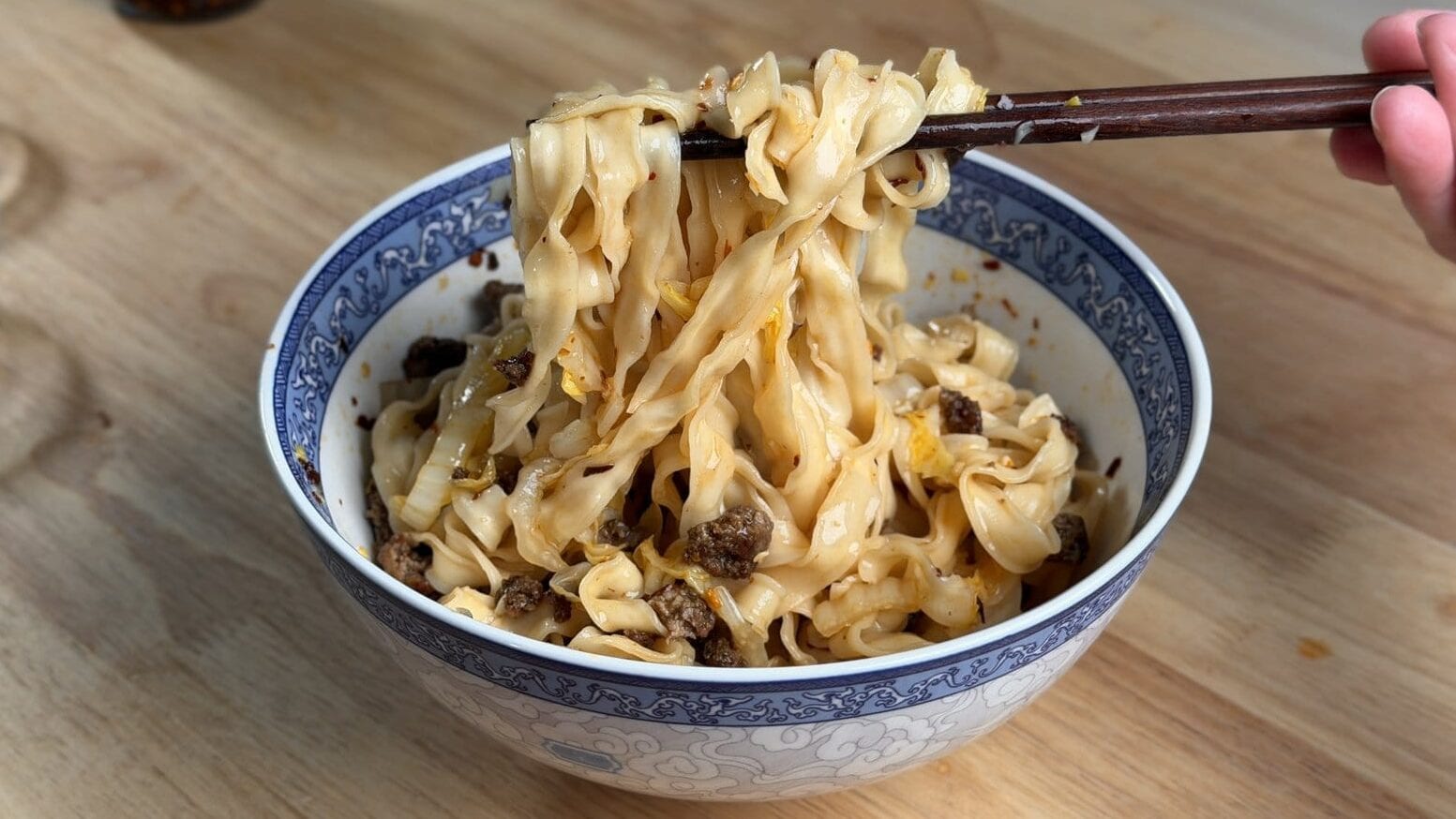 Hand pulling a bite of easy chili oil noodles with chopsticks from a bowl