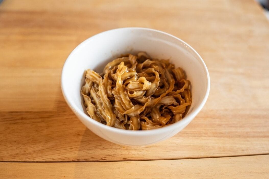 Top view of Fly By Jing Classic Soy Noodles prepared in a white bowl on wooden counter in the background
