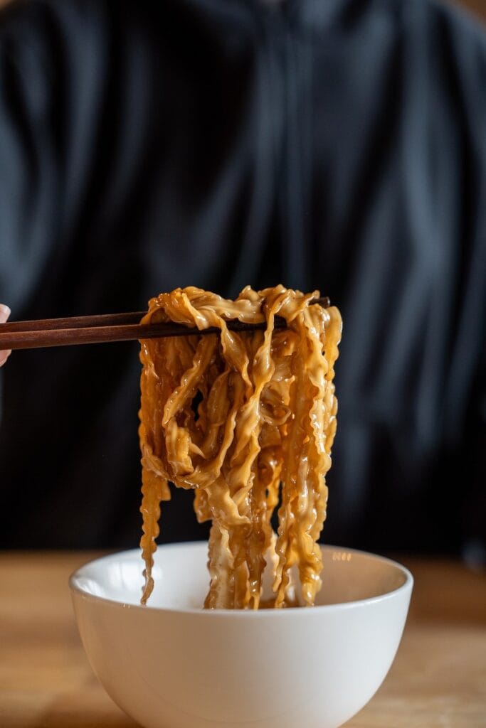 Fly By Jing Classic Soy Noodles being pulled with wooden chopsticks in a white bowl