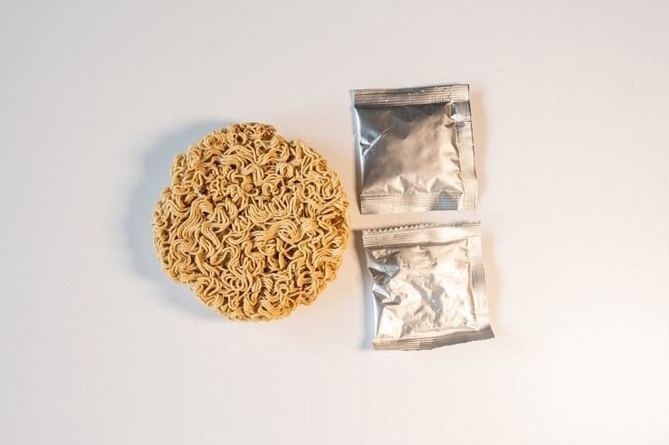 The contents of Heal Spot High Protein Instant Ramen Classic Ramen Flavor on a white surface. Circle noodle brick and 2 seasoning packets