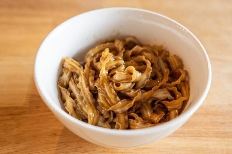 Top view of Fly By Jing Classic Soy Noodles prepared in a white bowl on wooden counter in the background