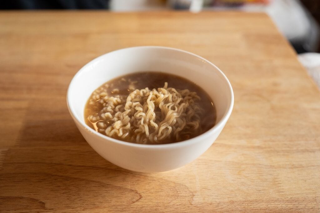 Maruchan Roast Beef Ramen Noodle Soup prepared in a white bowl, showing cooked wavy noodles in golden broth with a wooden surface background