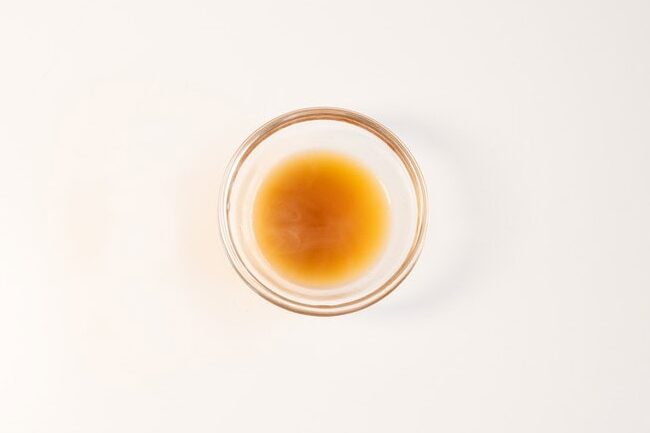 Golden brown broth or oil seasoning in a clear ramekin, light amber color