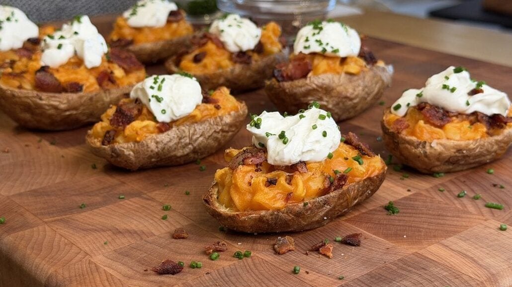 Seven loaded ramen baked potato halves spread across a butcher block, scattered with bacon crumbles and chives.