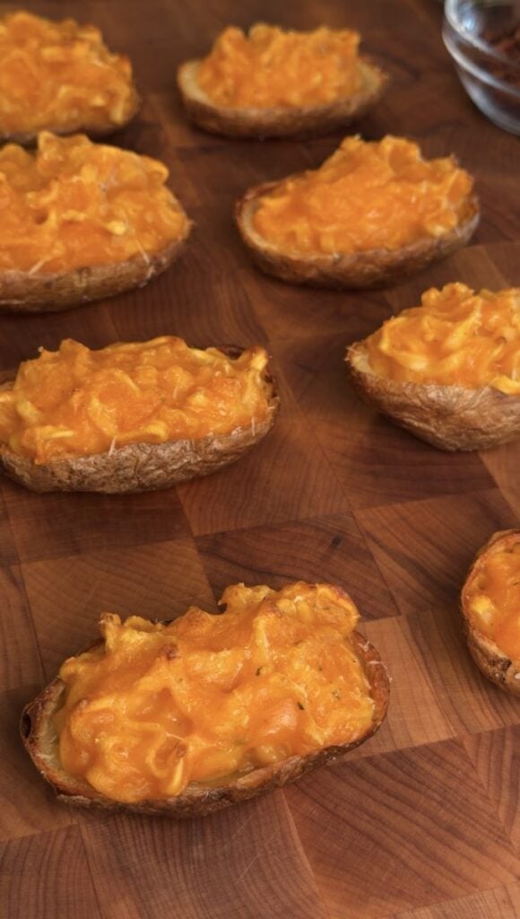 Potato shells filled with orange sauced ramen noodles on a butcher block, before the toppings go on.