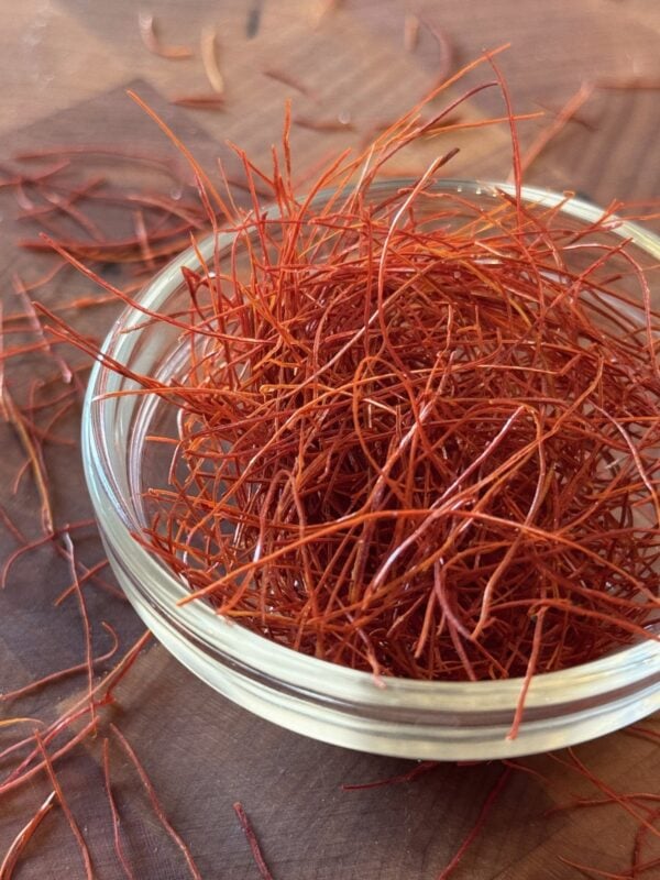 A small glass ramekin overflowing with bright red dried chili threads on a dark wooden cutting board.