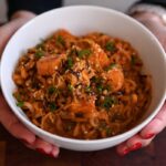 Hands holding a bowl of Creamy Cheesy Buldak Noodles with Imitation Crab