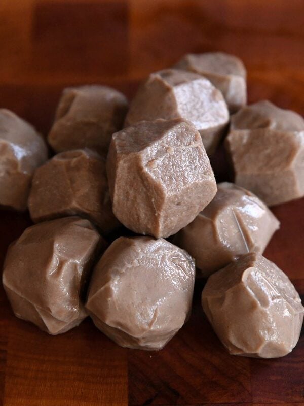 A pile of whole, smooth, and firm Vietnamese beef meatballs (bò viên) ready for slicing, resting on a dark walnut end-grain cutting board.