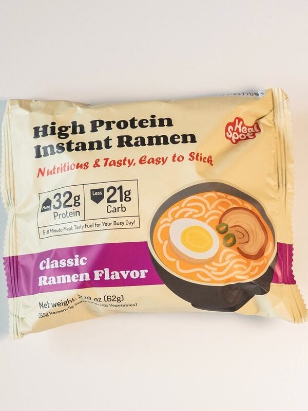 The cream and yellow Heal Spot High Protein Instant Ramen package on a white surface, showing the product name in black, a red Nutritious and Tasty tagline, 32g Protein and 21g Carb badges, and a purple Classic Ramen Flavor banner.