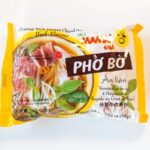 The yellow MAMA Pho Bo Beef Noodle Soup pack on a white table, with brown PHO BO lettering and a photo of beef pho with basil.