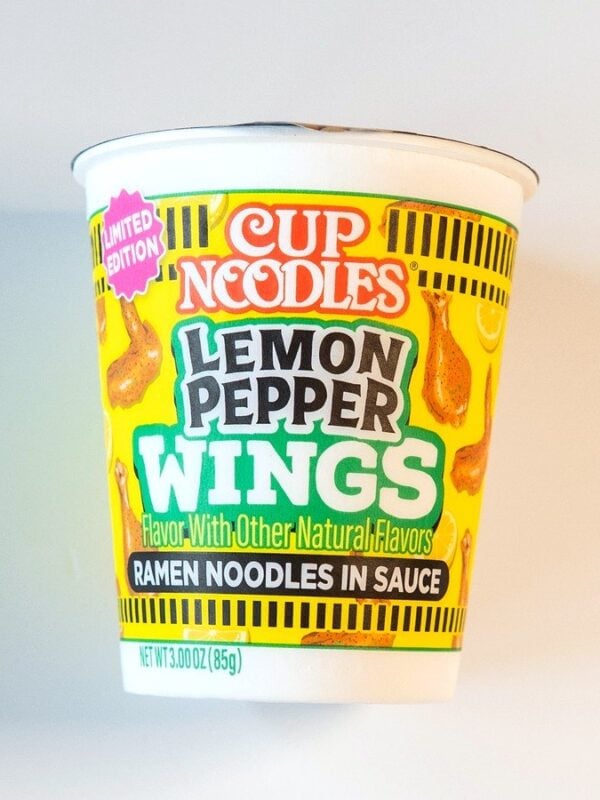 The yellow and green Nissin Cup Noodles Lemon Pepper Wings cup on a white table, with LEMON PEPPER WINGS in green letters and a pink Limited Edition badge.