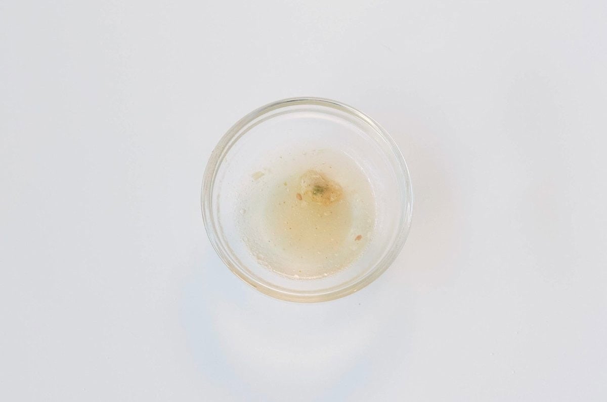 A small glass ramekin of the Ve Wong Mushroom Pork Instant Noodle Soup broth on a white surface, showing a thickened cloudy amber broth with visible oil droplets and tiny flecks of pork and seasoning.